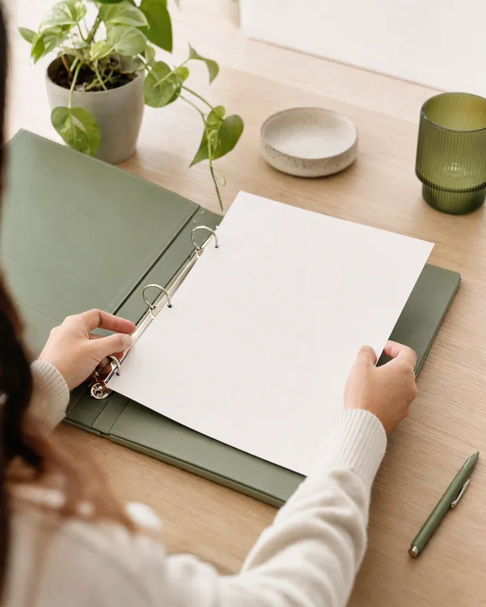 Hands filing a confirmation sheet into a sage-green ring binder